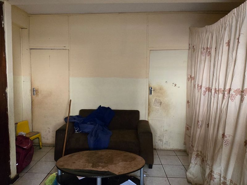 A living room area featuring tiled flooring and built-in storage, currently showing significant signs of wear and requiring cosmetic updates to improve its condition.