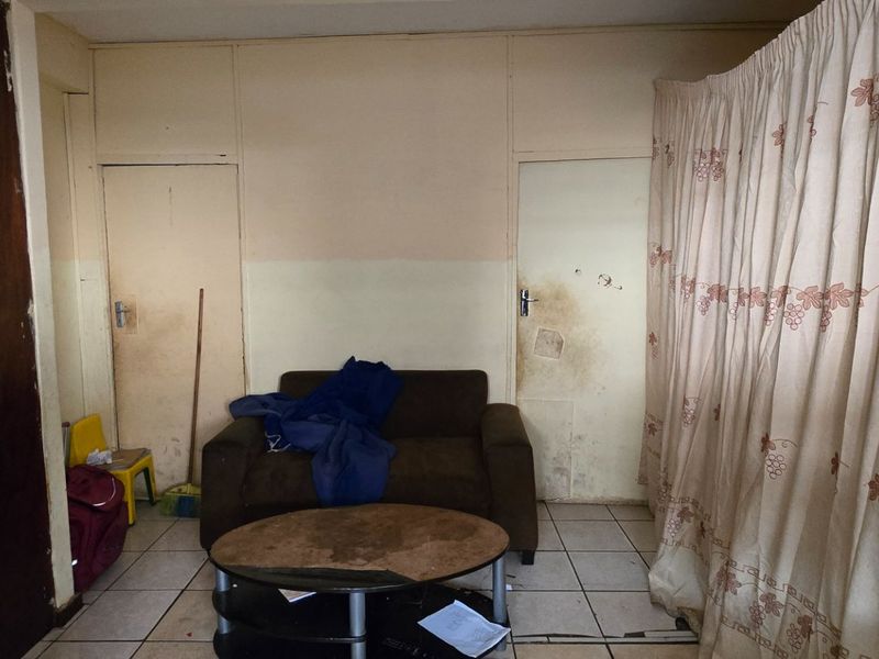 A living room area featuring tiled flooring and built-in storage, currently showing significant signs of wear and requiring cosmetic updates to improve its condition.
