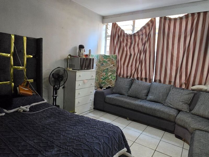 A bedroom featuring tiled flooring and a large window, currently used as a multi-purpose living and sleeping space.