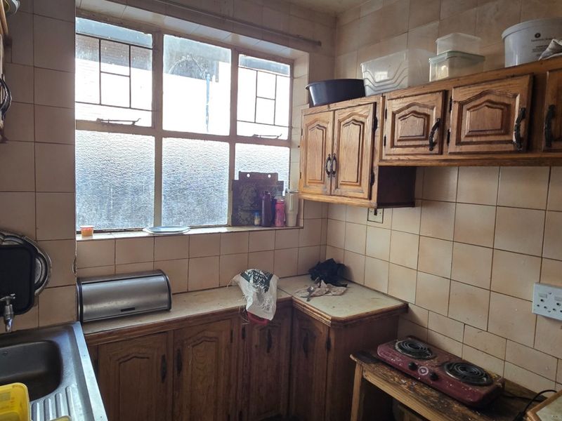 A compact kitchen featuring traditional wooden cabinetry, tiled backsplash, and a stainless steel sink, offering potential for a modern renovation.