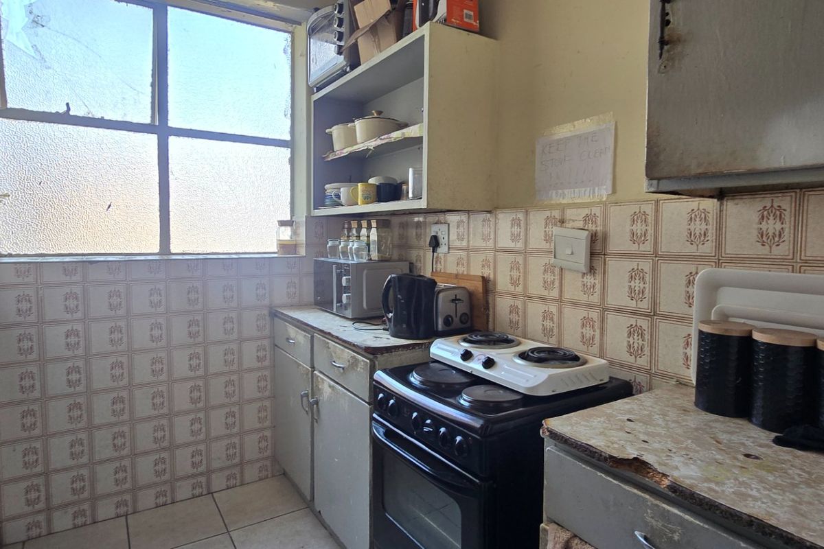 A dated kitchen featuring original tiled backsplash, built-in cabinetry, and a freestanding stove, requiring modernization to improve functionality and aesthetic appeal.