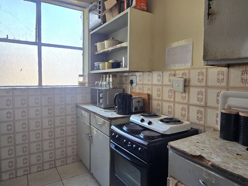 A dated kitchen featuring original tiled backsplash, built-in cabinetry, and a freestanding stove, requiring modernization to improve functionality and aesthetic appeal.