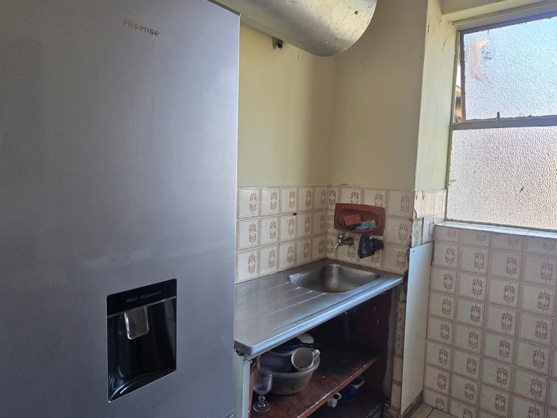 A compact kitchen area featuring a stainless steel sink, tiled splashbacks, and a window with a broken pane, requiring maintenance and cosmetic updates.