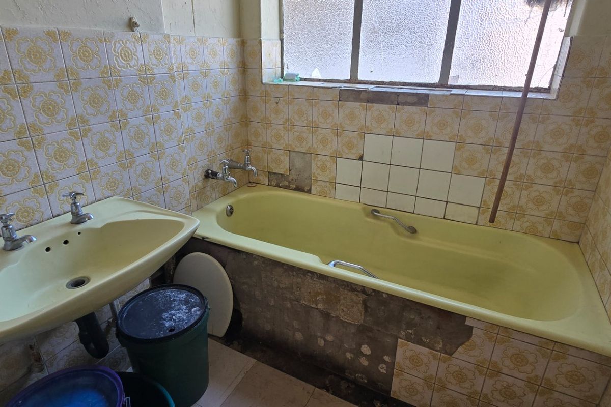 A dated bathroom featuring original yellow sanitaryware and patterned wall tiles, currently requiring significant renovation and repair to the wall finishes.