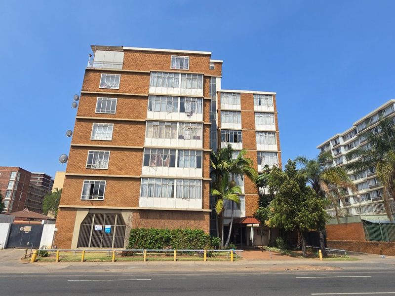 Front exterior view of a multi-story brick apartment building featuring enclosed balconies and a secure ground-level entrance.