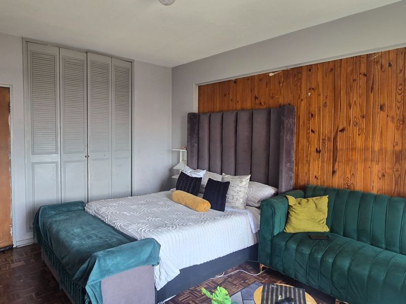 Bedroom featuring parquet flooring, built-in cupboards, and a timber-paneled feature wall, offering a functional space with potential for cosmetic updates.
