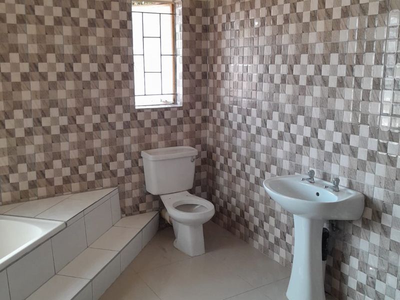 A functional bathroom featuring a pedestal basin, toilet, and a built-in bathtub with tiled walls and flooring.