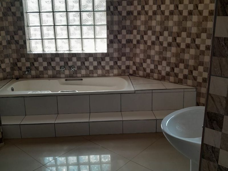 A bathroom featuring a built-in bathtub with tiled surround, a pedestal basin, and a glass block window with patterned wall tiling.
