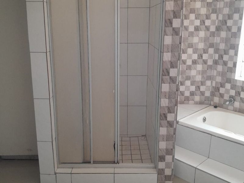 A functional bathroom featuring a built-in bathtub and a separate shower enclosure with tiled finishes throughout.