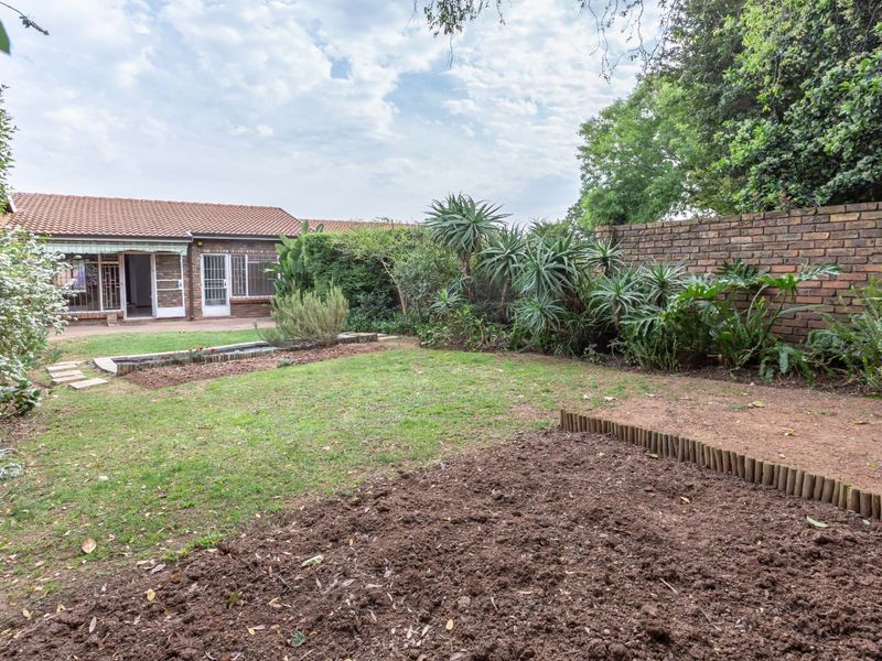 A private rear garden featuring a lawn, established garden beds, and a brick boundary wall, providing a quiet outdoor space for the townhouse.