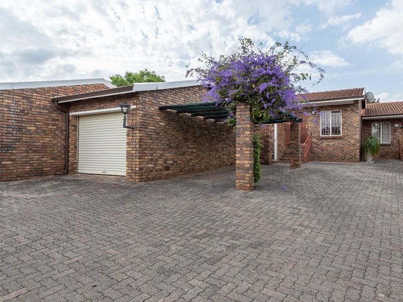 Front exterior view of a face brick townhouse featuring a paved driveway, roll-up garage, and a covered carport area.