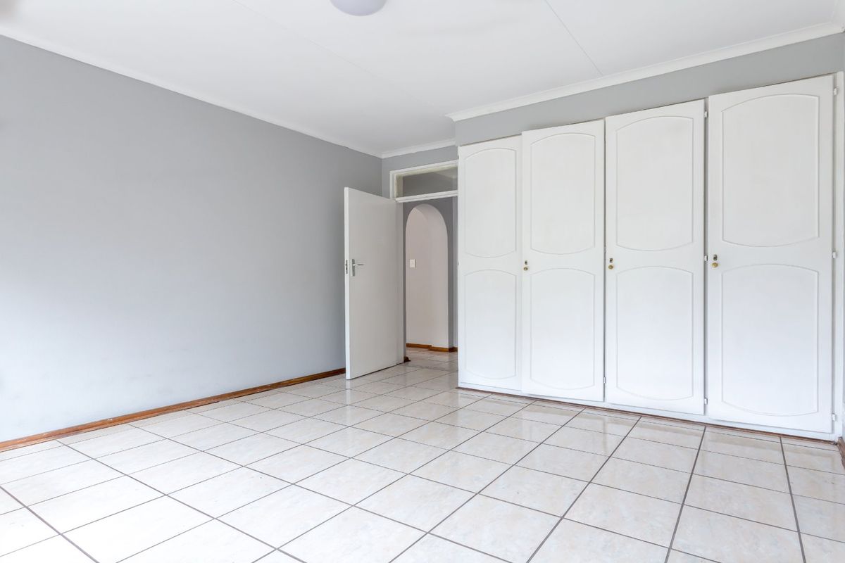 A bright, empty bedroom featuring neutral grey walls, tiled flooring, and ample built-in cupboard storage space.