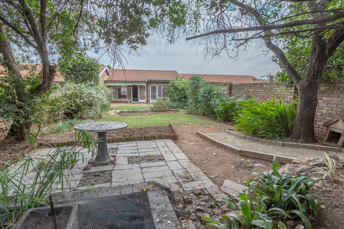 A private rear garden featuring a paved patio area, established trees, and a brick boundary wall, providing a quiet outdoor space for the townhouse.