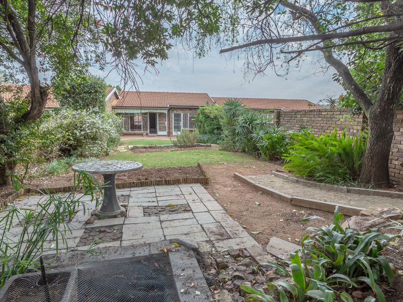A private rear garden featuring a paved patio area, established trees, and a brick boundary wall, providing a quiet outdoor space for the townhouse.