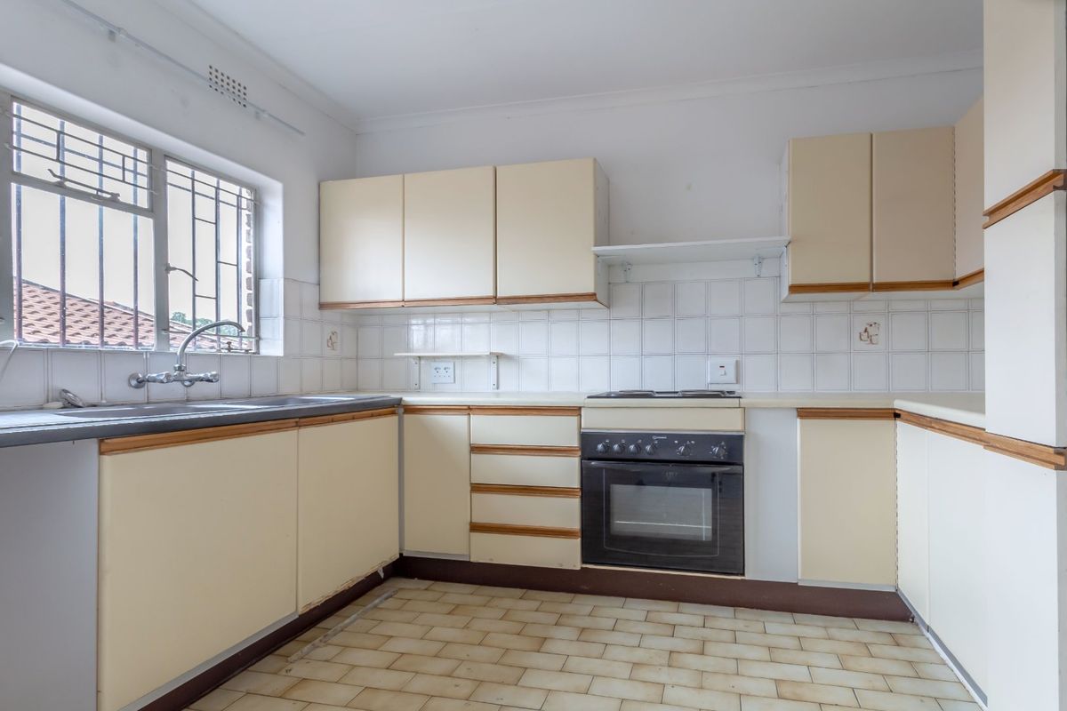 A functional, empty kitchen featuring built-in cabinetry, a built-in oven with hob, and a stainless steel sink, offering potential for modern renovation.
