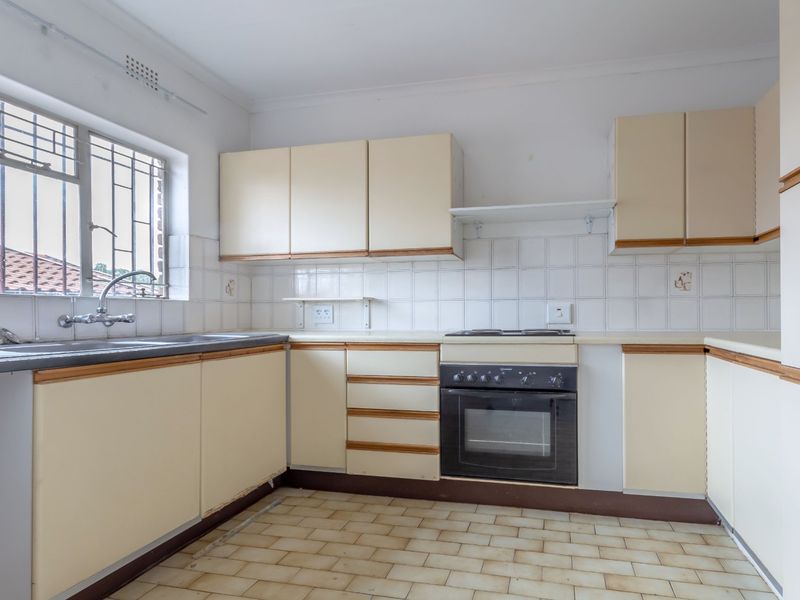 A functional, empty kitchen featuring built-in cabinetry, a built-in oven with hob, and a stainless steel sink, offering potential for modern renovation.