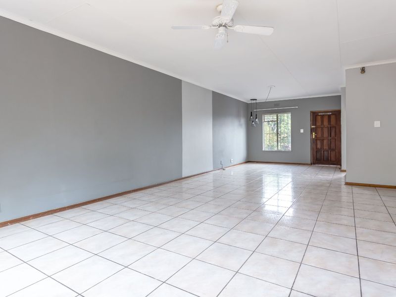 Spacious open-plan living area featuring neutral grey walls, tiled flooring, a ceiling fan, and a secure wooden entrance door.