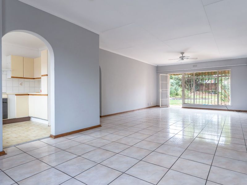 Spacious open-plan living area with tiled floors, ceiling fan, and an arched entryway leading to a functional kitchen with built-in cabinetry.