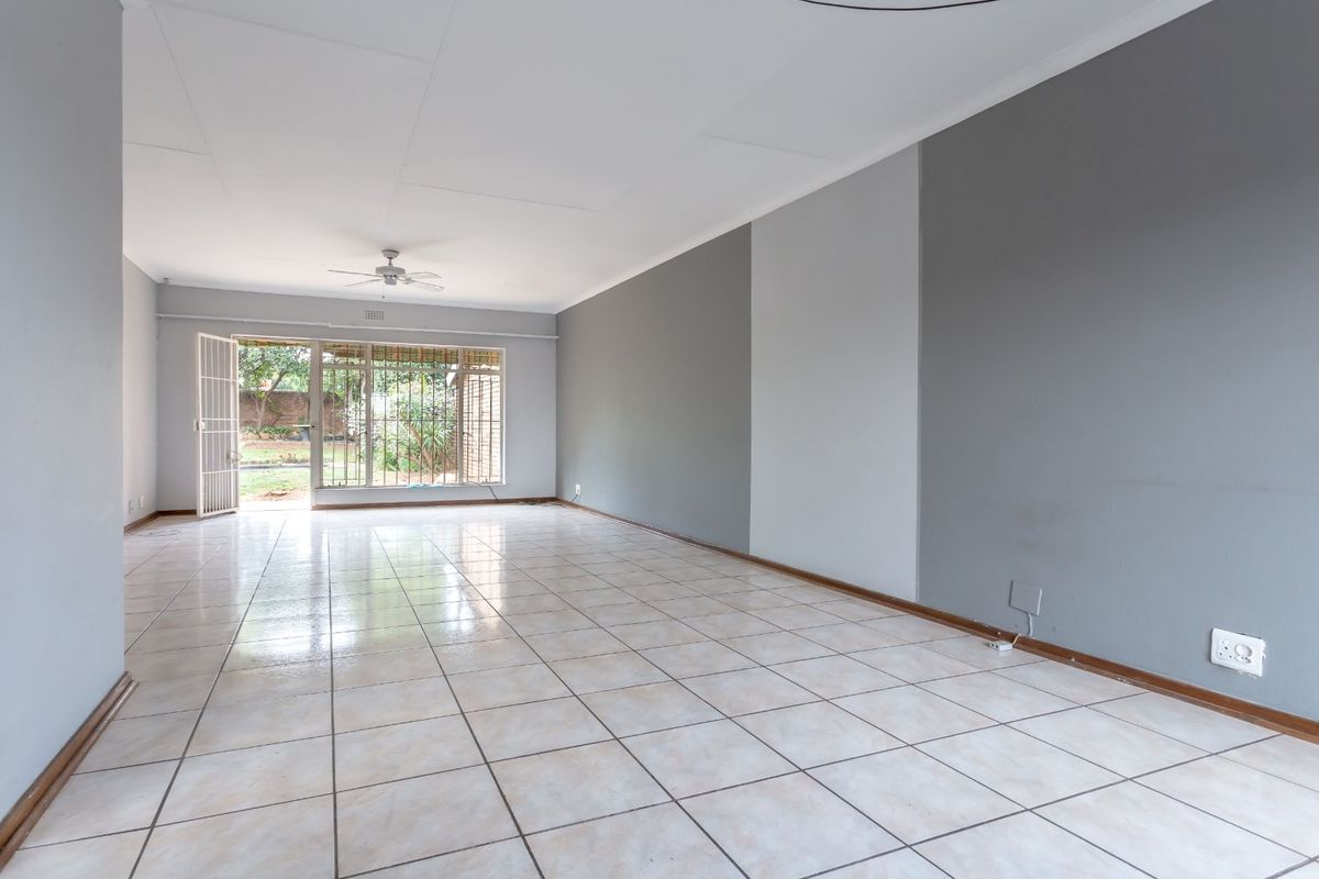 Spacious, empty living area featuring neutral tiled flooring, a ceiling fan, and direct access to the rear garden through a security-fitted sliding door.