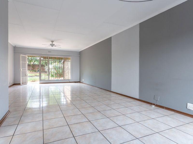 Spacious, empty living area featuring neutral tiled flooring, a ceiling fan, and direct access to the rear garden through a security-fitted sliding door.