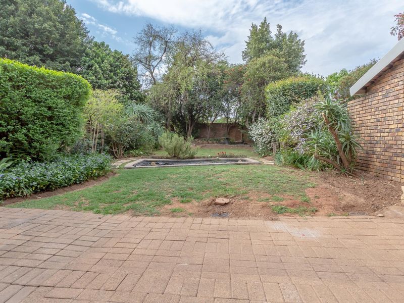A rear garden featuring a paved patio area, a central lawn with a small pond, and established perimeter landscaping with brick boundary walls.