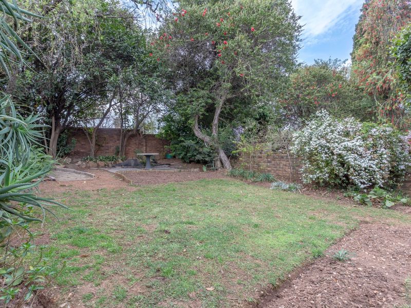A private rear garden featuring mature trees, established shrubs, and a brick boundary wall, offering a quiet outdoor space.