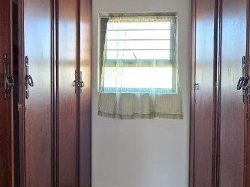 A narrow hallway featuring extensive built-in wooden cabinetry and tiled flooring, providing ample storage space.