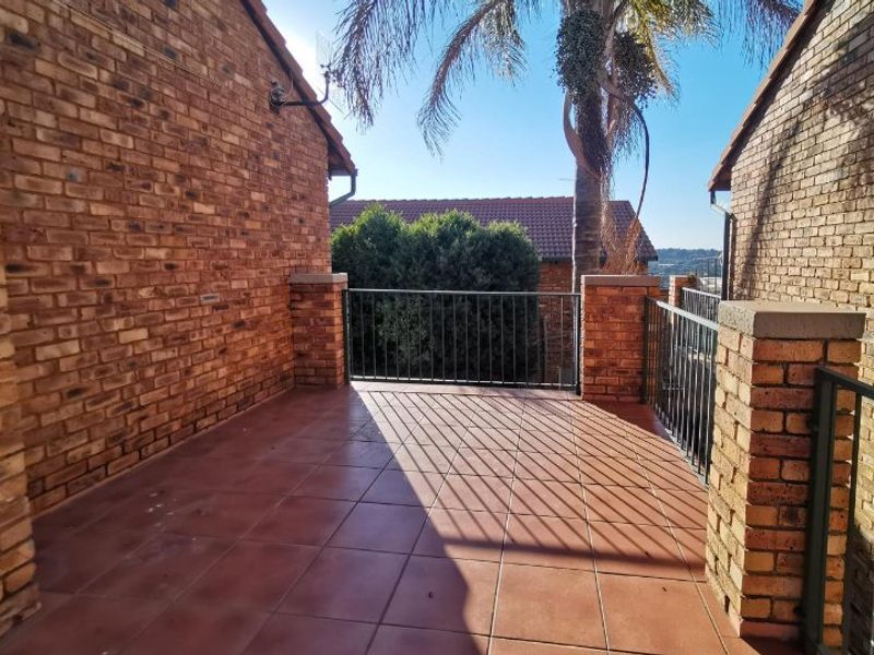 An open-air balcony featuring face brick walls, tiled flooring, and a metal balustrade, offering a private outdoor space.