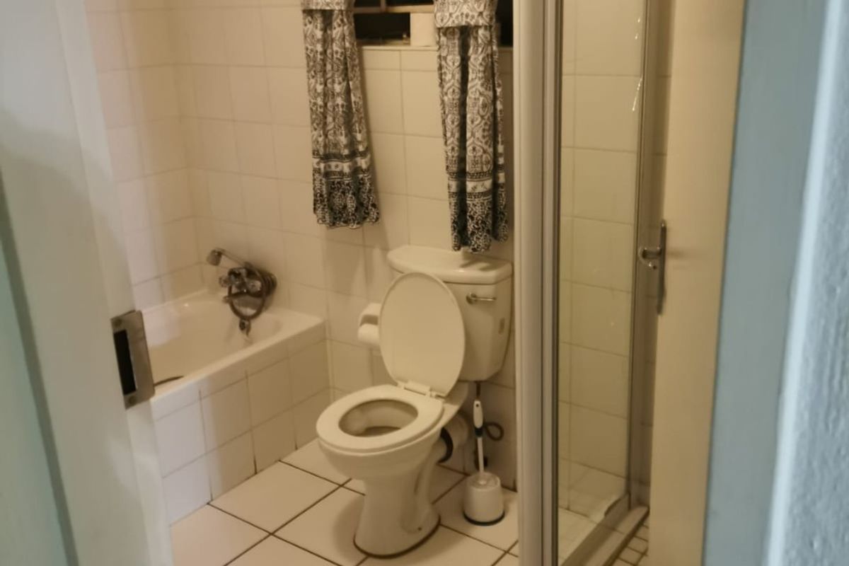 A functional bathroom featuring a bathtub, separate shower enclosure, and toilet with white tiled finishes throughout.