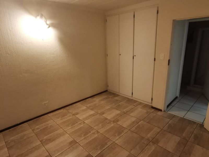 An empty bedroom featuring tiled flooring and built-in cupboards, offering a clean and neutral space ready for personalization.