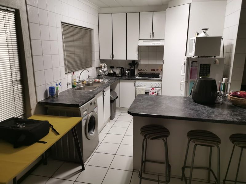 Functional kitchen featuring white cabinetry, dark laminate countertops, tiled splashbacks, and a breakfast bar, providing a practical layout for daily meal preparation.