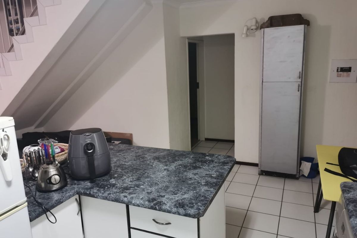 A functional kitchen area featuring laminate countertops, built-in cabinetry, and ceramic floor tiles, situated beneath an internal staircase.