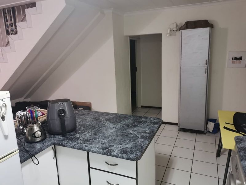 A functional kitchen area featuring laminate countertops, built-in cabinetry, and ceramic floor tiles, situated beneath an internal staircase.