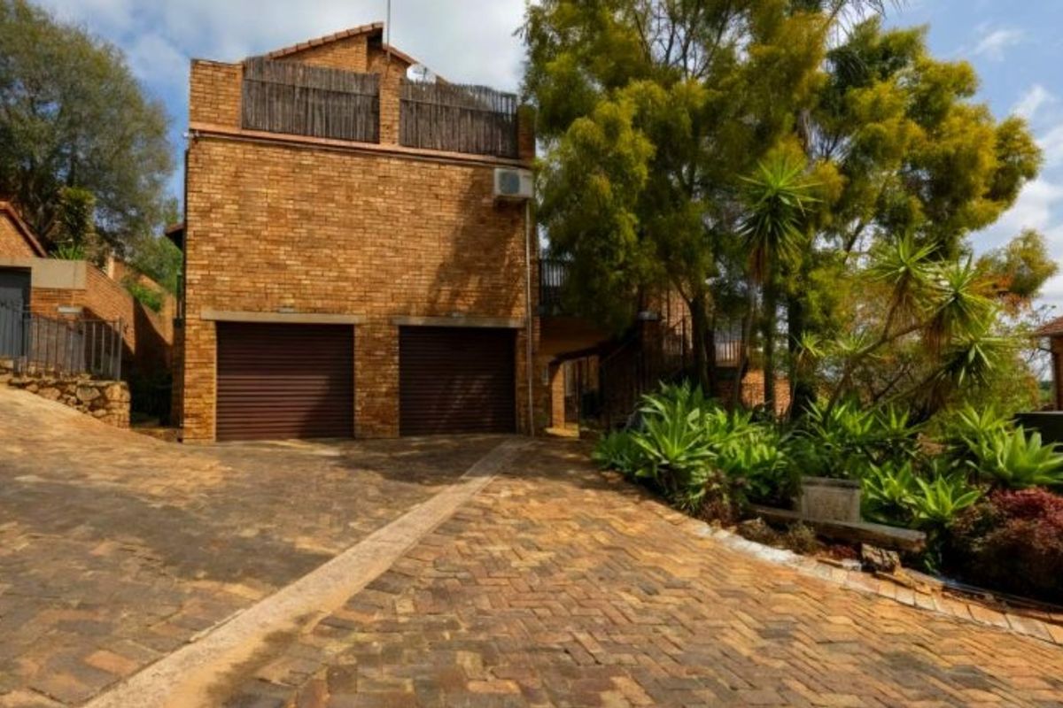 Front view of a double-story townhouse featuring a double garage, brick exterior, and a paved driveway with established garden landscaping.