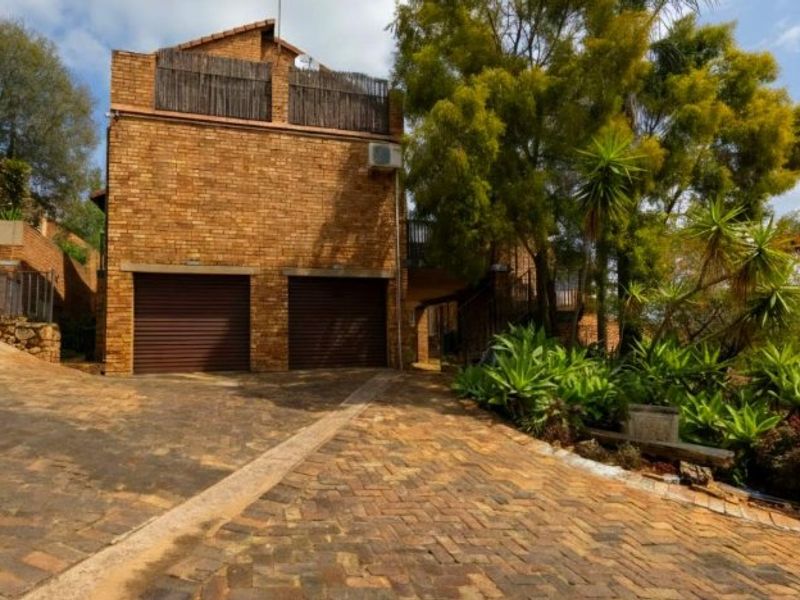 Front view of a double-story townhouse featuring a double garage, brick exterior, and a paved driveway with established garden landscaping.