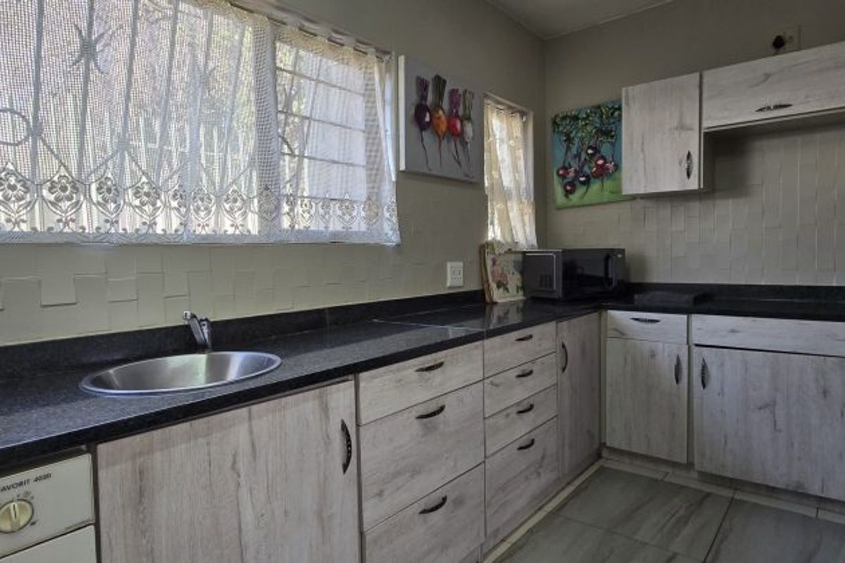 A functional kitchen featuring light wood-grain cabinetry, dark granite countertops, a stainless steel sink, and tiled backsplash with neutral floor tiles.