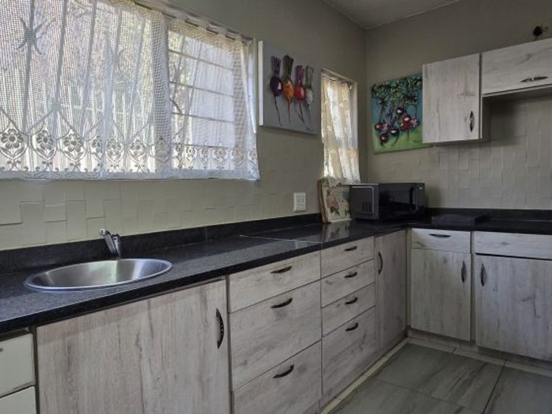 A functional kitchen featuring light wood-grain cabinetry, dark granite countertops, a stainless steel sink, and tiled backsplash with neutral floor tiles.