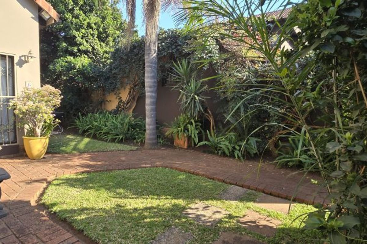 A private rear garden featuring a brick-paved pathway, established landscaping, and a secure entrance to the main dwelling.