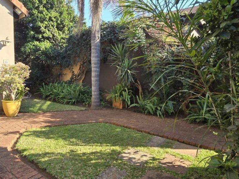 A private rear garden featuring a brick-paved pathway, established landscaping, and a secure entrance to the main dwelling.
