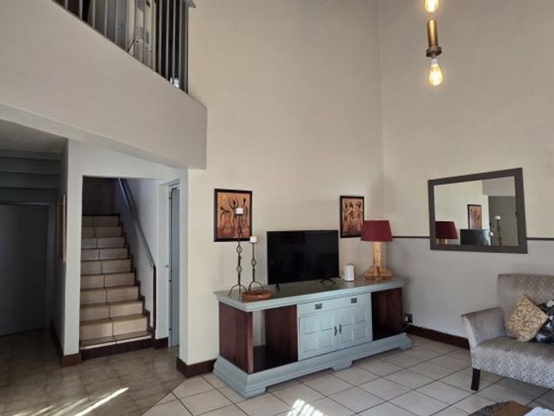 Spacious living area featuring high ceilings, a mezzanine level, tiled flooring, and a staircase leading to the upper floor.