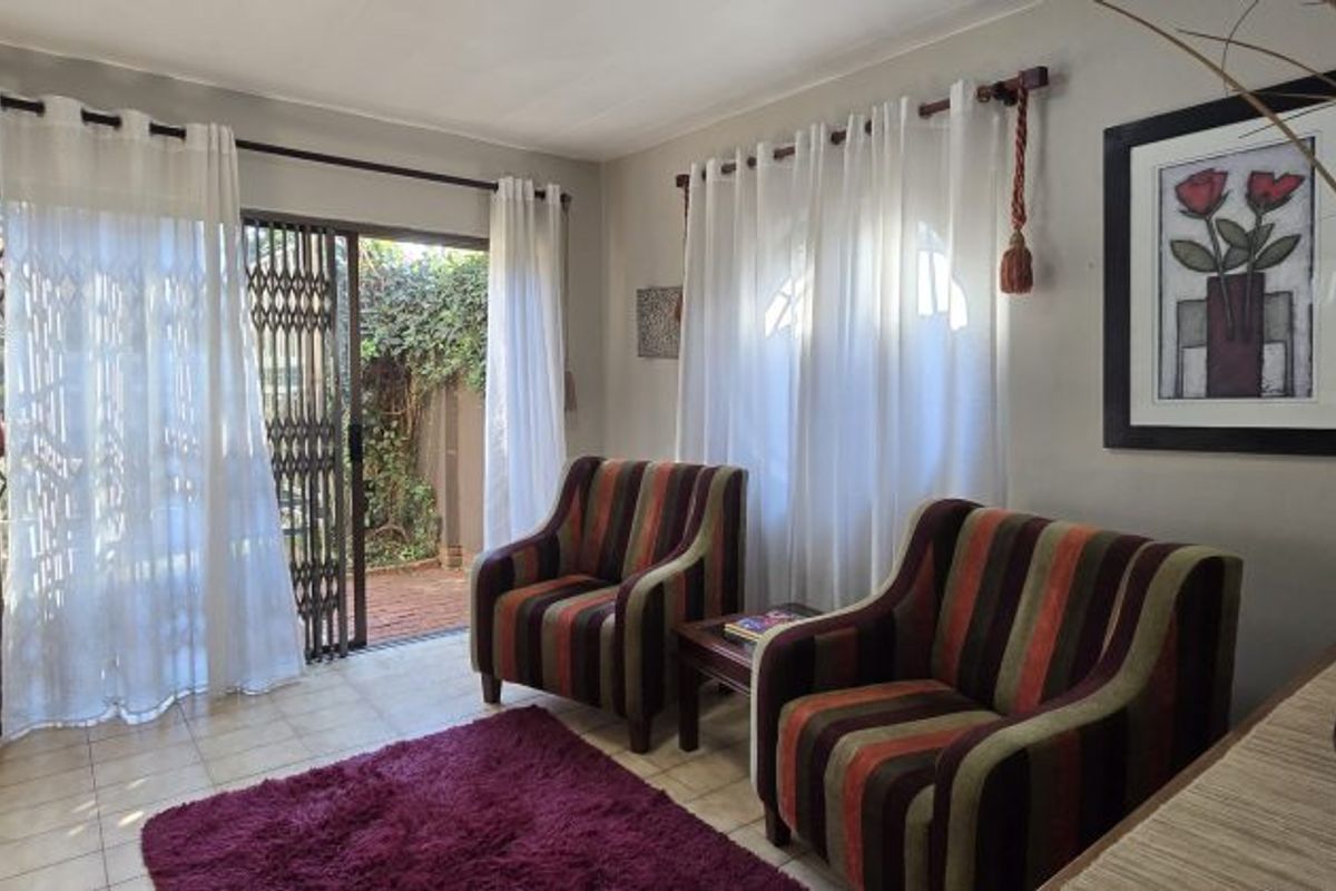 A bright living room featuring tiled flooring and a sliding glass door with security gate providing direct access to the outdoor area.