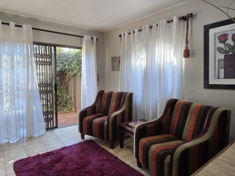 A bright living room featuring tiled flooring and a sliding glass door with security gate providing direct access to the outdoor area.