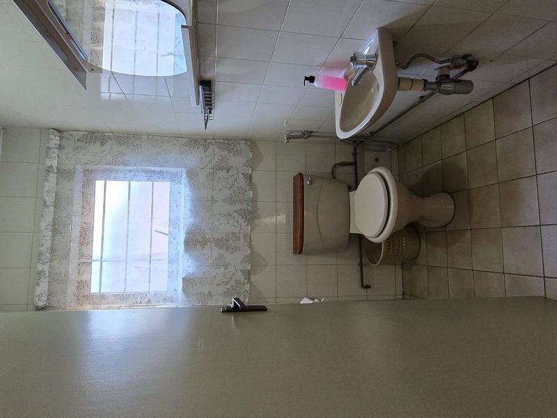 A functional bathroom featuring a wall-mounted basin, toilet, and tiled finishes. The space is dated and would benefit from modern updates.