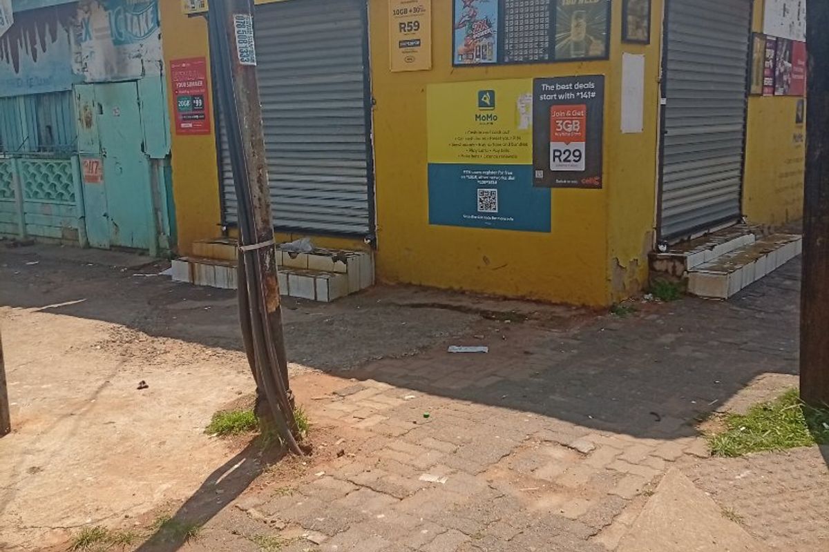 Street-level view of a commercial corner property featuring yellow exterior walls, metal roller shutters, and concrete entrance steps.