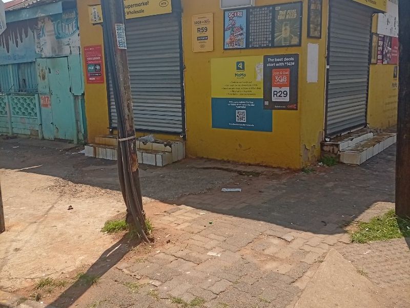 Street-level view of a commercial corner property featuring yellow exterior walls, metal roller shutters, and concrete entrance steps.
