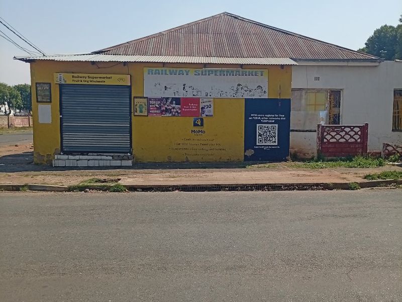 Front elevation of a commercial retail building featuring a corrugated metal roof, roller shutter entrance, and prominent street-facing signage.