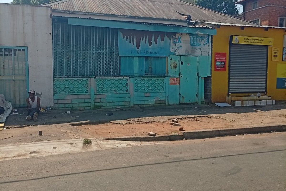 Street-level view of a commercial property featuring a corrugated metal roof, security shutters, and a weathered facade requiring maintenance.