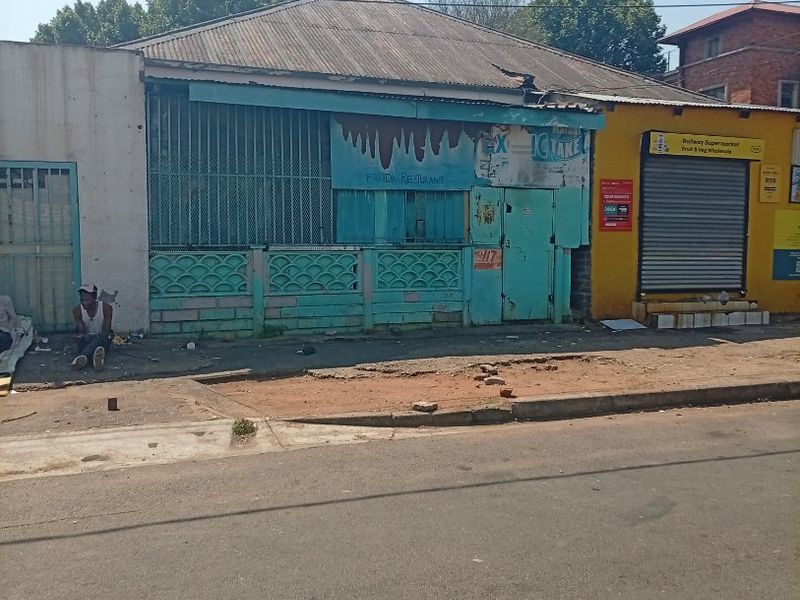 Street-level view of a commercial property featuring a corrugated metal roof, security shutters, and a weathered facade requiring maintenance.