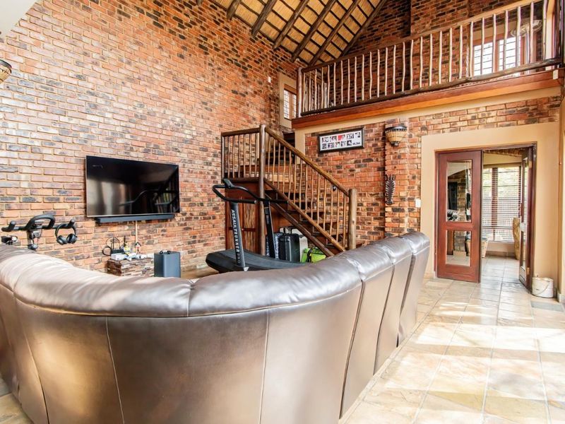 Spacious living area featuring exposed brick walls, a high thatched ceiling, timber staircase, and mezzanine level, creating a rustic and open atmosphere.
