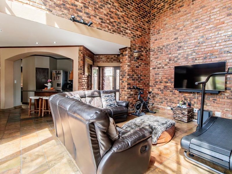 Spacious open-plan living area featuring high ceilings, exposed brick walls, and tiled flooring, with a seamless transition to the kitchen area.